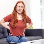 Woman Suffering Back Pain Sitting On The Couch At Home Stock Photo 385x215.jpg